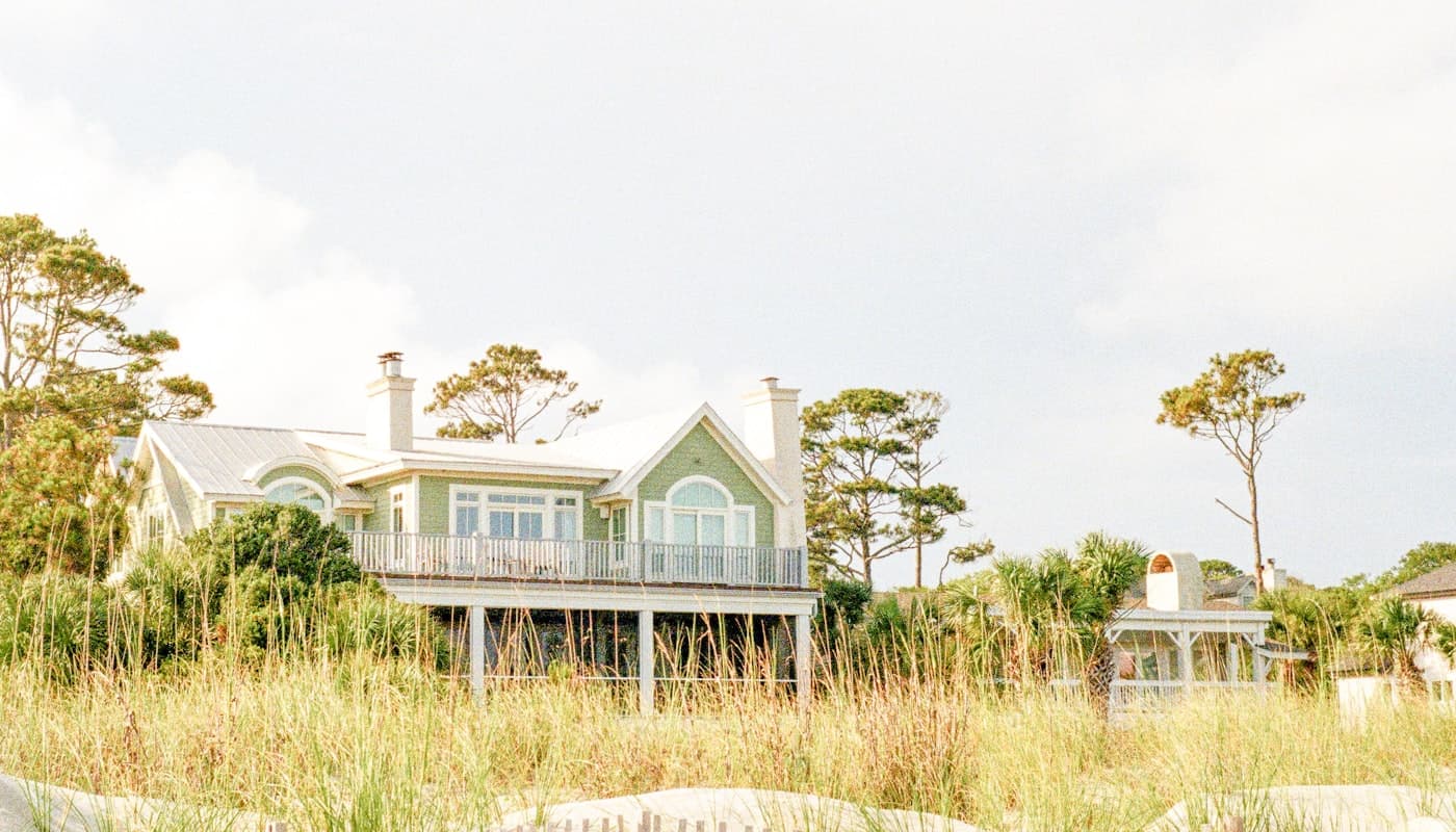 Green and white shingle cottage with a white fence and lush summer lawn — classic coastal East End architecture